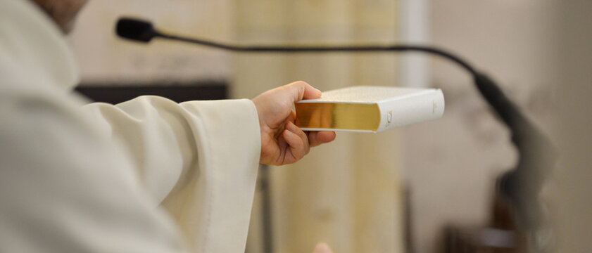 Un pr&ecirc;tre tend le livre de la Bible dans sa main, lors d'une c&eacute;r&eacute;monie dans une &eacute;glise