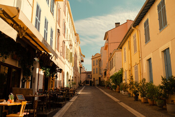 Fototapeta premium Charming European street with outdoor cafes, colorful facades and potted plants. Sunny day in a Mediterranean town, travel and lifestyle inspiration.
