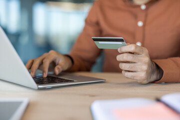 Fototapeta premium Person making a secure digital payment with a credit card on a laptop keyboard, representing e-commerce, banking transactions, and internet finance technology for purchasing goods and services