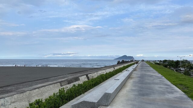 A serene view of Guishan Island from the coastal pathway, showcasing the ocean and distant landscape under a cloudy sky, Toucheng, Taiwan.