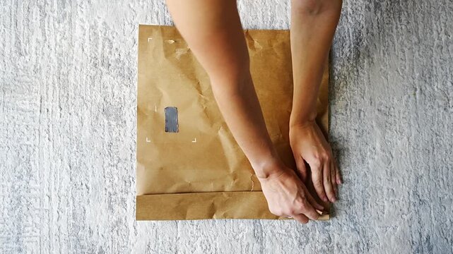 Top view of woman opening package and checking clothing item inside at home. Receiving delivery process, online shopping experience and sustainable packaging moment.