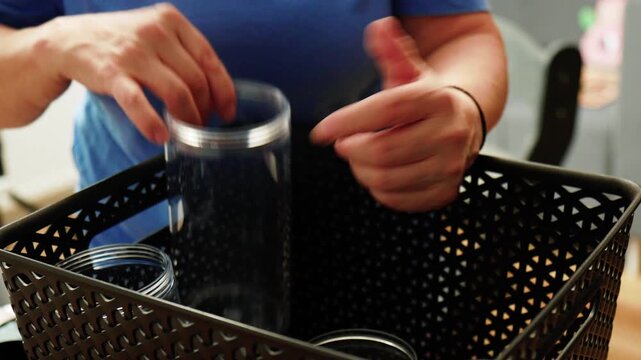 Hands placing a glass container into a basket in a home setting with natural light