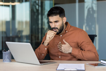 Young businessman experiencing discomfort and sickness, grabbing his chest and coughing while...