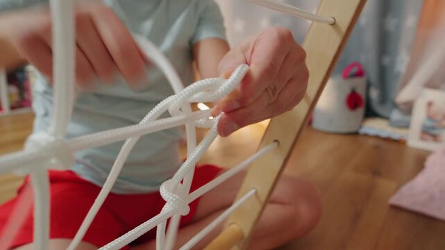 Person ties knots on a wooden ladder during an indoor activity in a bright room with colorful toys in the background