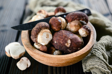 Obraz premium Fresh wild porcini mushrooms and knife in wooden bowl on rustic wooden table
