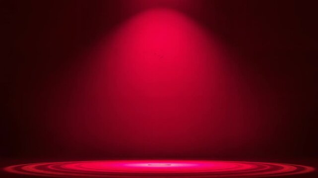 Widening overhead spotlight forming concentric rings and bright disk on center stage, red backdrop