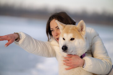 A woman hugs an Akita dog in a snowy landscape, both smiling and enjoying the moment