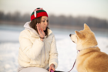 A woman hugs an Akita dog in a snowy landscape, both smiling and enjoying the moment