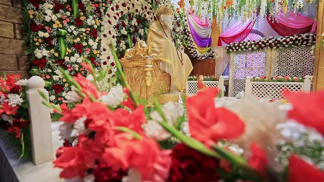 A pan shot of Sai Baba or Sai Ram idol surrounded by floral decorations inside the temple