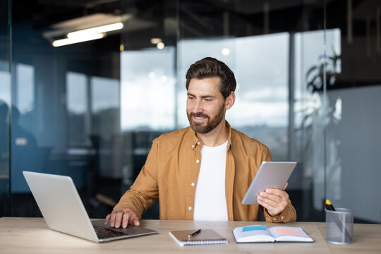 Person working on a laptop and holding a digital tablet, navigating multiple screens for efficient remote work and productivity in a contemporary business environment