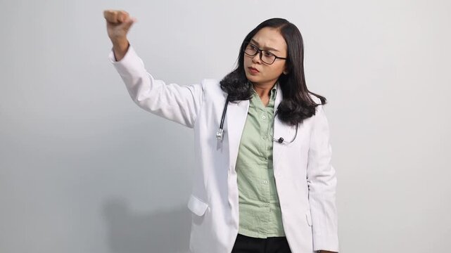 Beautiful female doctor showing serious, angry, or unhappy expression, crossed hand gesture and thumb down facing sideways in empty space.