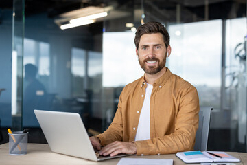 Smiling man enjoying a productive day, typing on a laptop at a contemporary desk in a bright office...