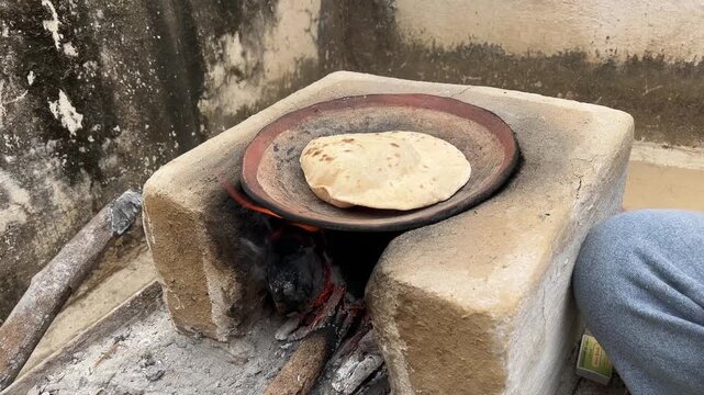 Traditional Indian flatbread (roti) being cooked on a clay stove or chulha using firewood