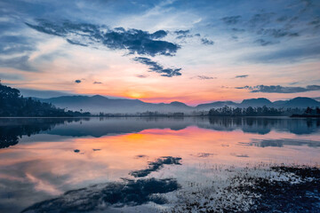 Peaceful morning landscape with misty mountains and mirror-like water reflection.