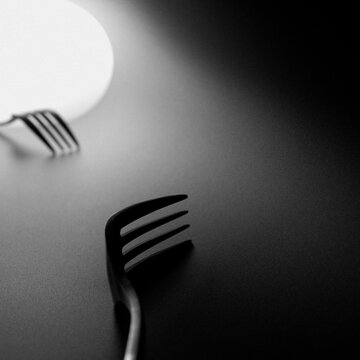 Deux fourchettes, l'une du c&ocirc;t&eacute; lumineux et l'autre du c&ocirc;t&eacute; obscur. Photographie en noir et blanc avec effet granuleux