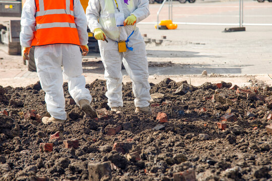 Two workers in protective gear remove asbestos from contaminated ground
