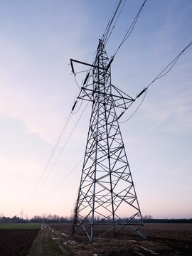 High voltage transmission tower and power lines over rural farmland at dusk with copy space, symbol of electricity supply, power grid infrastructure and energy network.