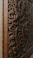 Naklejka premium Intricate wooden carving with floral and swirling patterns, showcasing detailed craftsmanship and rich texture. dark wood exudes antique and elegant feel, highlighting artistic skill