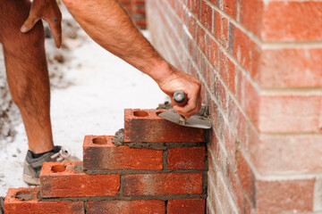 Close-up of Skilled bricklayer laying bricks with trowel on construction site