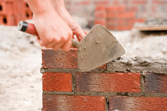 Close-up of Skilled bricklayer laying bricks with trowel on construction site