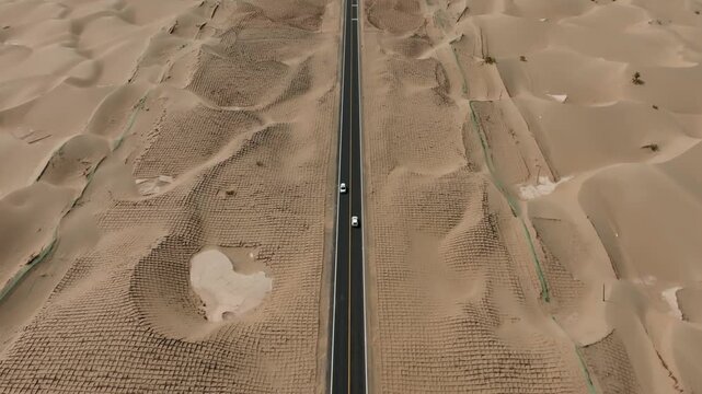 Aerial view of a straight road cutting through the textured desert landscape, with a vehicle visible on the road, Hotan Prefecture, China.