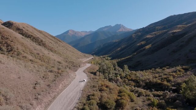 Aerial view of a solitary car winding through a mountain road with rugged terrain and vegetation, Saty, Almaty Region, Kazakhstan.