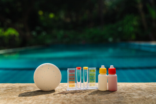  Pool water testing kit with chlorine tablet and reagent bottles on pool edge for swimming pool maintenance, chemical balance, and water quality control 