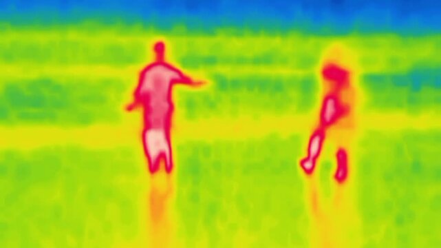 A couple of young people walking on the beach. Image from thermal imager device.