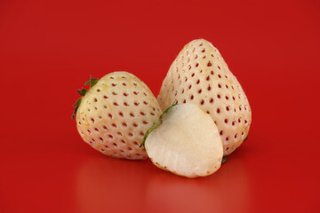 Unique pineberry strawberries with white flesh and red seeds on a vibrant red background