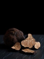 Black truffle with sliced pieces arranged on a dark surface. Gourmet food ingredient for culinary dishes.