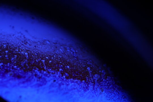 Abstract macro shot of blue liquid bubbles and a thin fluid thread. Artistic deep blue lighting creating a futuristic and scientific atmosphere. High-contrast texture with focus on surface tension 
