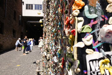 Obraz premium Close-up view of the famous Gum Wall in Seattle’s Post Alley, with visitors walking through the narrow passageway near Pike Place Market.