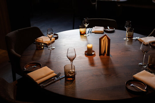 Detail of an interior of a restaurant with wine glasses and a table, napkins and candles.