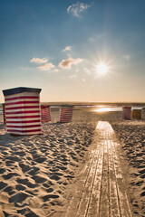 Fototapeta premium Traditional Striped Beach Tents on Borkum Island at Sunset with Wooden Path