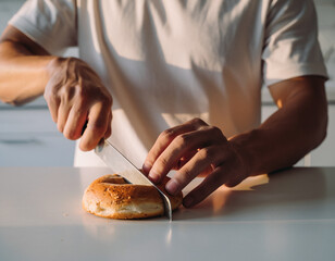 A person slicing a fresh bagel on a kitchen counter in warm morning light.