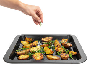A hand sprinkles herbs over roasted potatoes on a black baking tray.