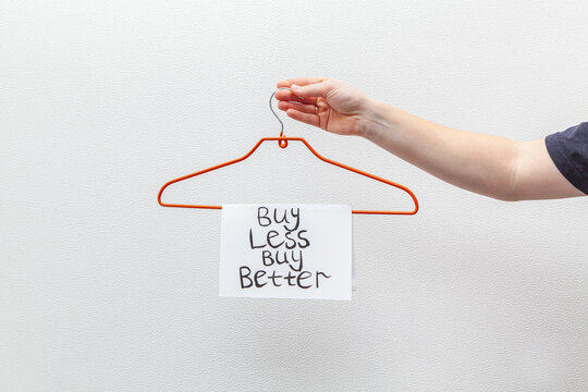 Man holds orange hanger with inscription on the sheet "Buy less buy better". The concept of reasonable consumption