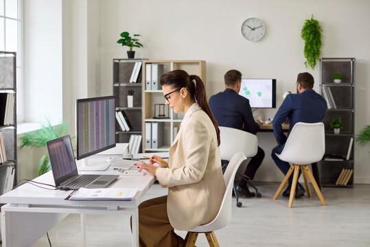 Accountant conducts audit analysis on office computer. Woman uses calculator, reviews spreadsheet data, checks accuracy and compliance in bright office. Teamwork and finance operations concept.