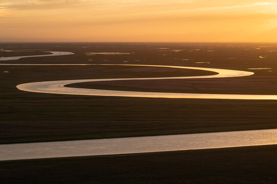 Aerial view of a serpentine river glimmers golden under the setting sun, cutting through the dark earth, Ba Yin Guo Leng Meng Gu Zi Zhi Zhou, Xin Jiang Wei Wu Er Zi Zhi Qu, China.