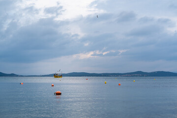 Fishing boat floats in calm water as clouds gather over the horizon during twilight hours © Anastasia Bruzinsky