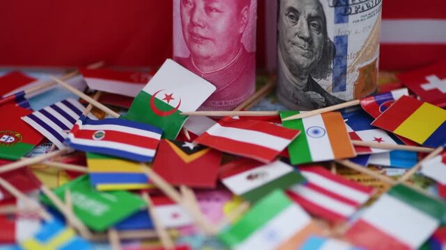 A macro close up of a roll of US dollar bills and Chinese Yuan bank notes on top of a pile of small country flags, with the Chinese and American national flags in the background. A China, US economic,