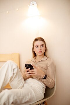 Beautiful smiling woman using her phone bedroom chair. A relaxing moment in a cozy bedroom.