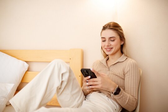Beautiful smiling woman using her phone bedroom chair. A relaxing moment in a cozy bedroom.