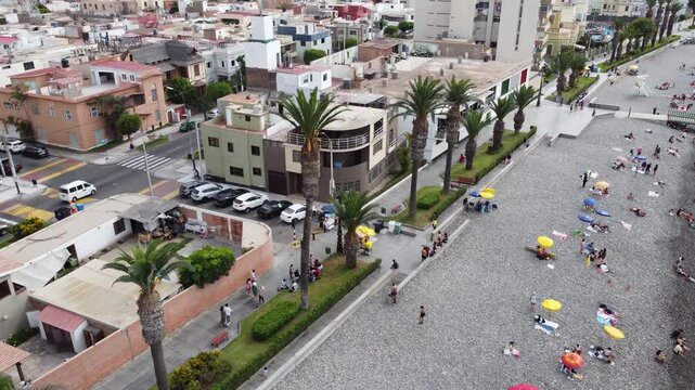 aerial view crowded pebble beach Callao with families and vendors, colorful umbrellas dotting rocky