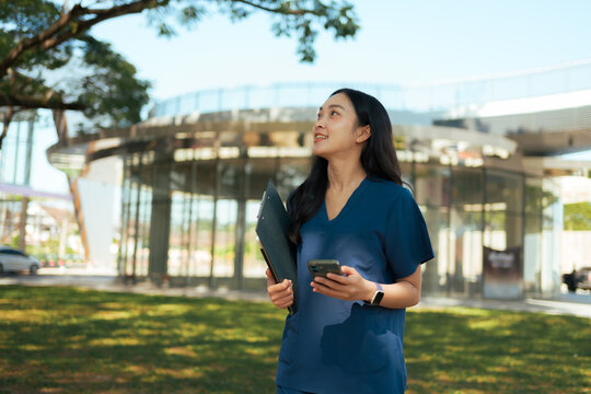 Female doctor holding clipboard and mobile phone outside hospital