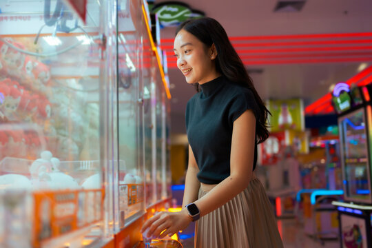 Young woman playing claw machine in bright arcade center