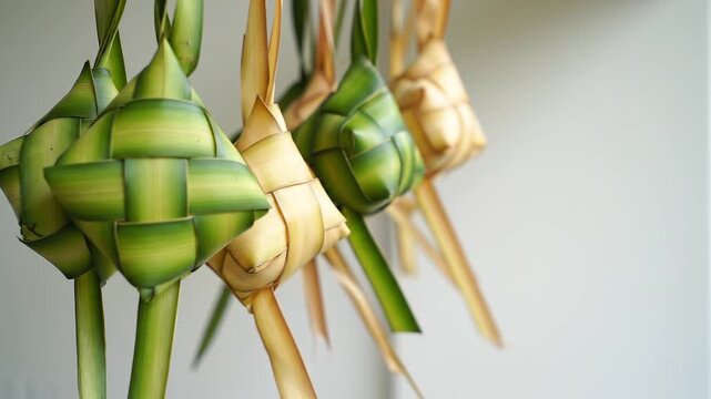 Close-up of intricately woven ketupat or rice dumplings made from palm leaves on a blurred white background.