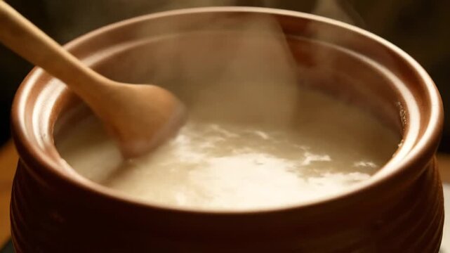 Stirring hot creamy food in a clay pot