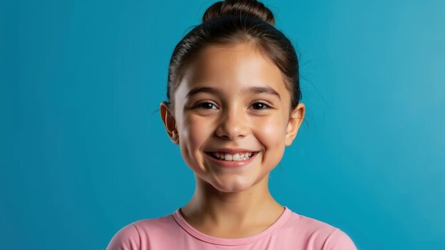 Portrait of a smiling young girl on a blue background. Happy child with hair in a bun wearing a pink t-shirt. Childhood happiness and positivity concept. Copy space for text