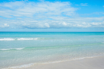 Calm ocean waves gently lap on the sandy shore under a bright blue sky